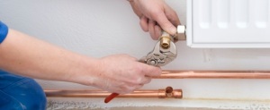 two hands of plumber with pliers and radiator